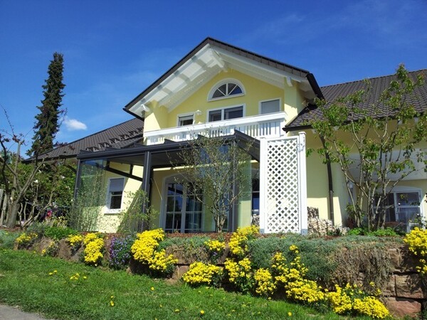 Modernes Einfamilienhaus mit gelber Fassade, Wintergarten und blühendem Garten im Frühling.