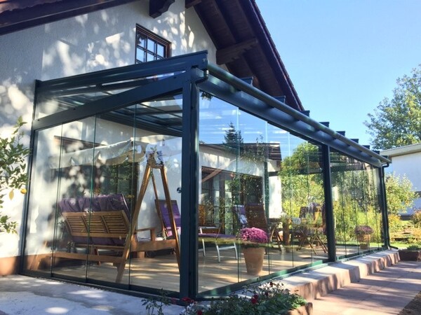 Moderner Wintergarten aus Glas mit gemütlicher Sitzgruppe am Einfamilienhaus im Garten.