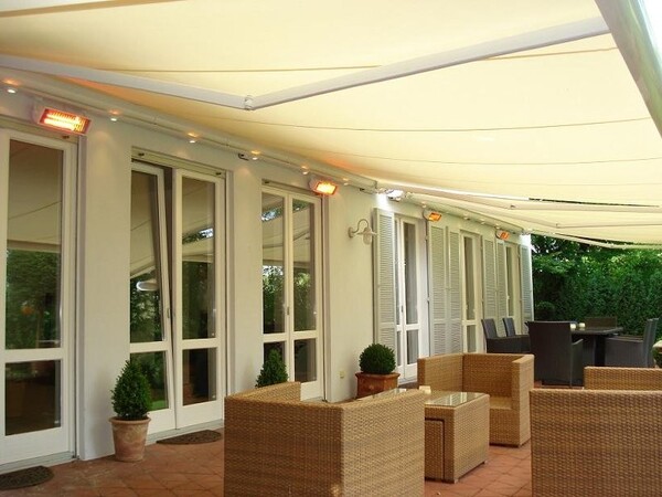 Überdachte Terrasse mit Markise, Gartenmöbeln und modernen Heizstrahlern am Haus.