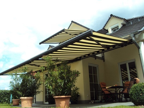 Moderne gelb-schwarze Markise beschattet Terrasse mit Gartenmöbeln an Einfamilienhaus.