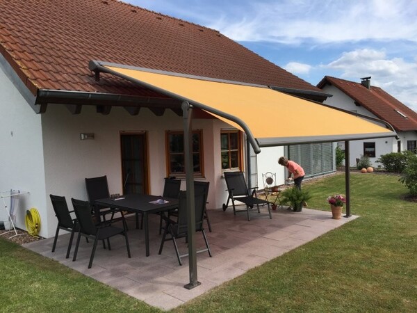 Überdachte Terrasse mit gelber Markise, Gartenmöbeln und gepflegtem Garten am Einfamilienhaus.