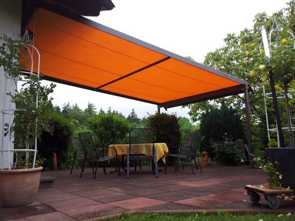 Überdachte Terrasse mit orangefarbener Markise, Gartenmöbeln und Blick ins Grüne.