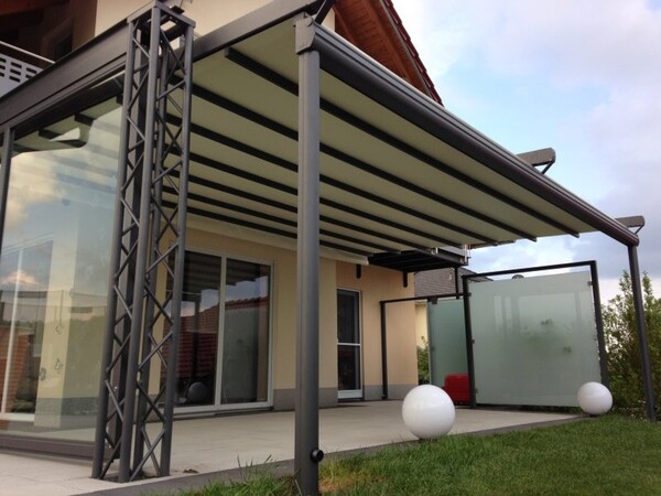 Moderne Terrassenüberdachung aus Glas und Aluminium an einem Einfamilienhaus im Garten.